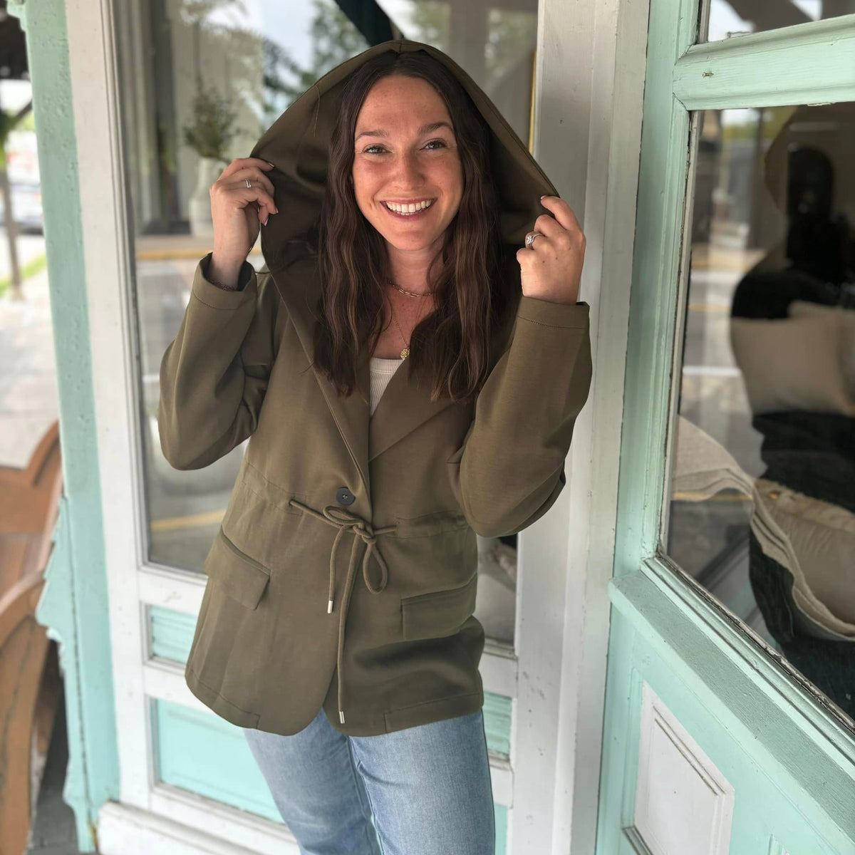 Woman wearing an olive utility jacket with hood outside the boutique